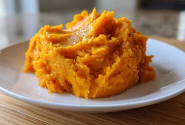 A close-up of a fluffy mound of bright orange mashed sweet potatoes topped with melted butter.