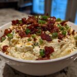 A close-up of creamy Million Dollar Dip served in a white bowl, generously topped with crumbled bacon and sliced green onions.