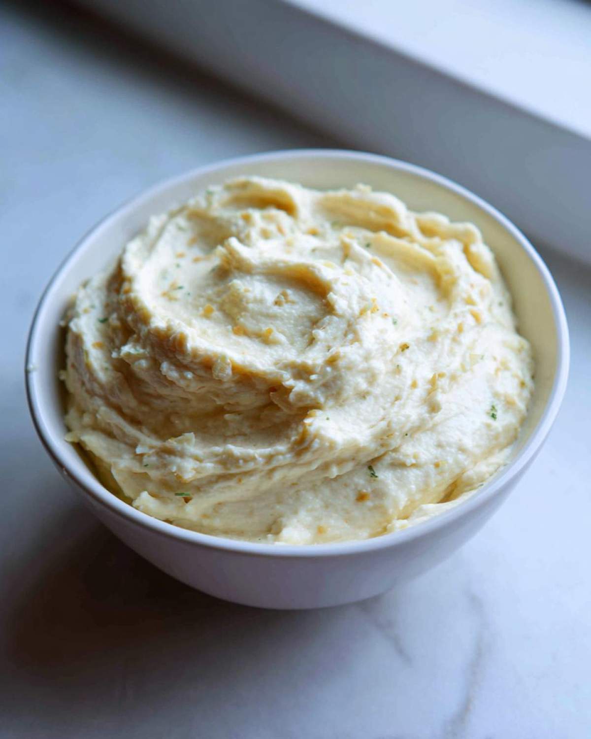A close-up of thick, creamy Olive Garden Alfredo Sauce seasoned with herbs in a white bowl.
