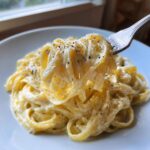 A fork lifting fettuccine generously coated in creamy Olive Garden Alfredo sauce and black pepper.