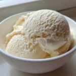 A close-up of several scoops of creamy, vanilla-colored protein ice cream served in a small white bowl.