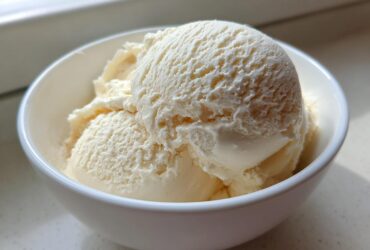 A close-up of several scoops of creamy, vanilla-colored protein ice cream served in a small white bowl.