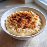 Close-up of creamy rice pudding in a white bowl, generously dusted with ground cinnamon.