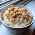 A close-up of creamy rice pudding in a white bowl, generously sprinkled with ground cinnamon.