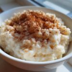 Close-up of a white bowl filled with creamy rice pudding, generously dusted with cinnamon.