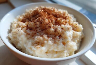 Close-up of a white bowl filled with creamy rice pudding, generously dusted with cinnamon.