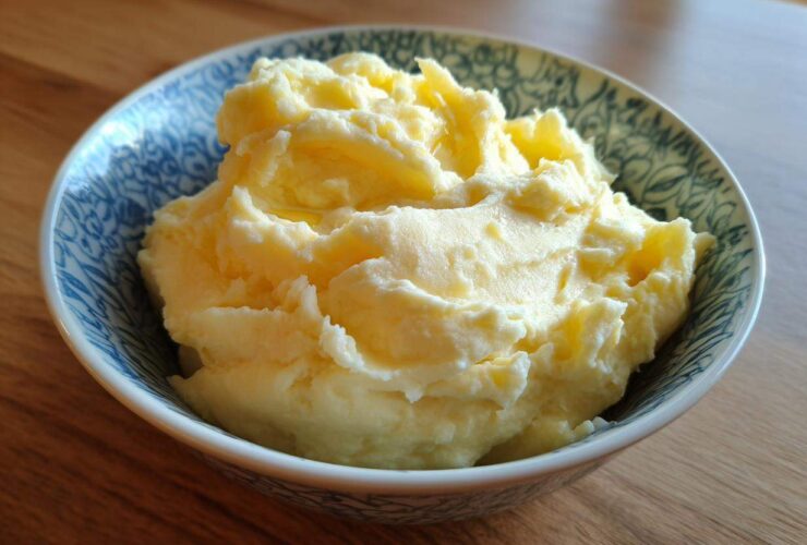 A close-up of creamy, fluffy roasted garlic mashed potatoes served in a decorative blue and white bowl.