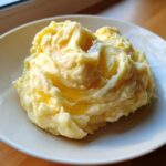 A close-up of fluffy roasted garlic mashed potatoes topped with melted butter pooling in the center.
