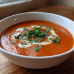 A close-up of a bowl of creamy tomato bisque, swirled with cream and topped with fresh basil.