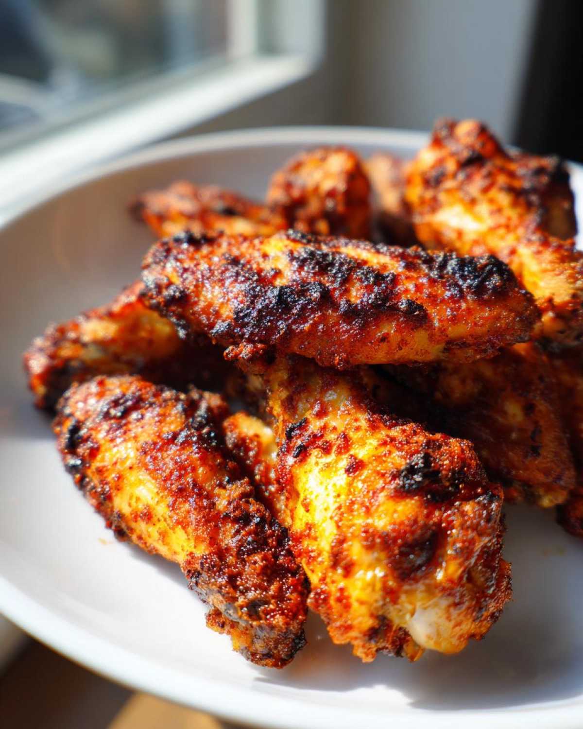 Close-up of perfectly seasoned and crispy air fryer chicken wings piled on a white plate.