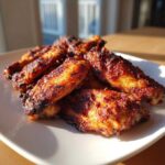 A close-up of several perfectly cooked, dark golden brown crispy baked chicken wings piled on a white square plate.