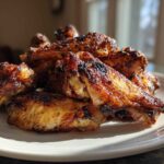 A close-up of perfectly cooked, intensely browned and crispy baked chicken wings piled high on a white plate.