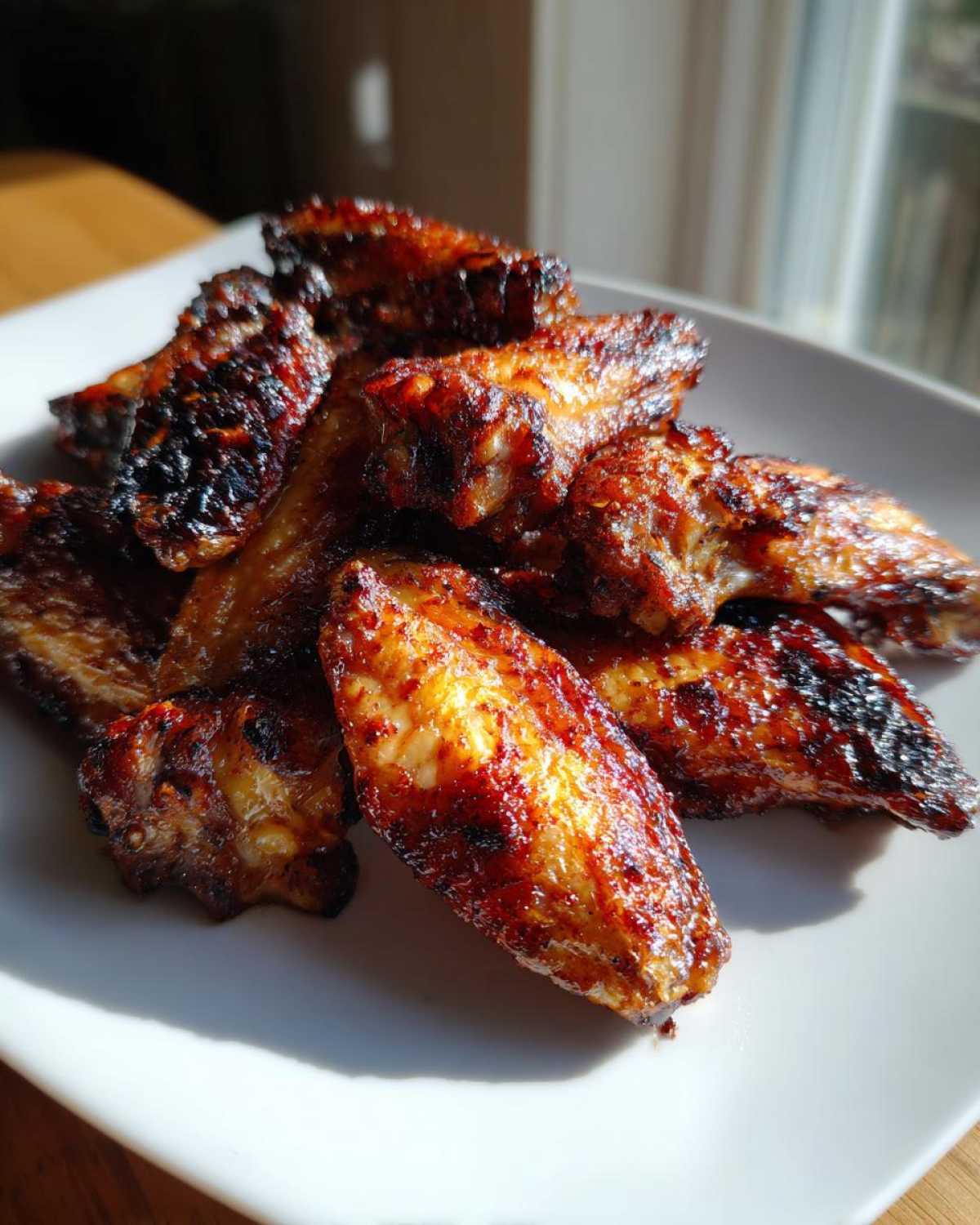A pile of glossy, deeply caramelized crispy baked chicken wings sitting on a white plate, highlighted by natural sunlight.
