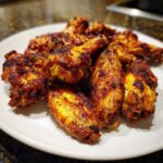 A close-up of perfectly crispy, seasoned chicken wings piled high on a white plate.