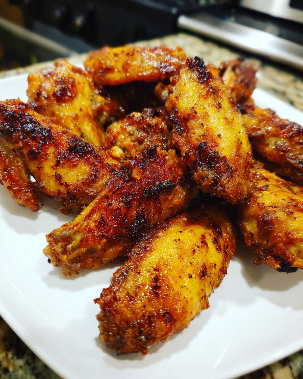 Close-up of perfectly crispy, seasoned chicken wings piled high on a white serving plate.