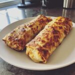 Two perfectly golden and crispy Chimichangas resting on a white plate, showing a nicely browned, bubbly exterior.