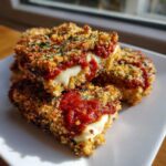 Close-up of stacked, crispy baked eggplant parmesan pieces showing melted mozzarella cheese and marinara sauce.