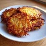 Close-up of four golden-brown, crispy potato latkes stacked slightly on a white plate.