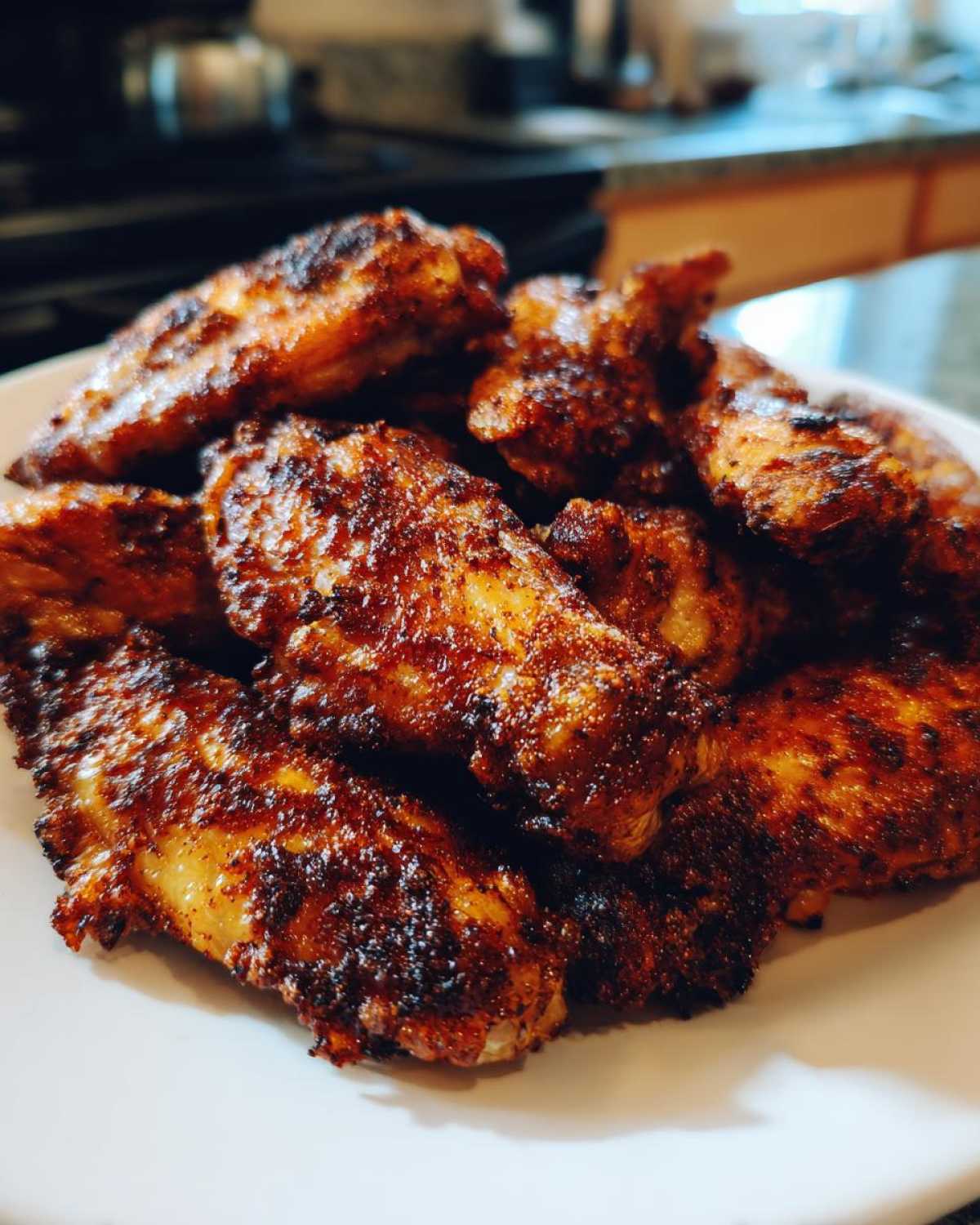 Close-up of a pile of perfectly crispy, seasoned chicken wings on a white plate.