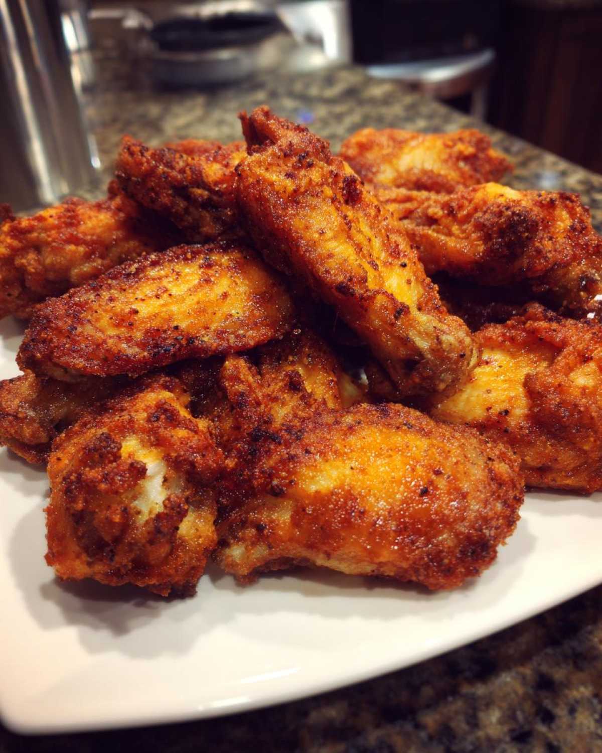 A close-up of a pile of perfectly crispy, seasoned chicken wings served on a white plate.