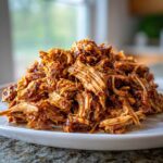 A close-up of a generous mound of saucy, shredded crock pot pulled pork piled high on a white plate.