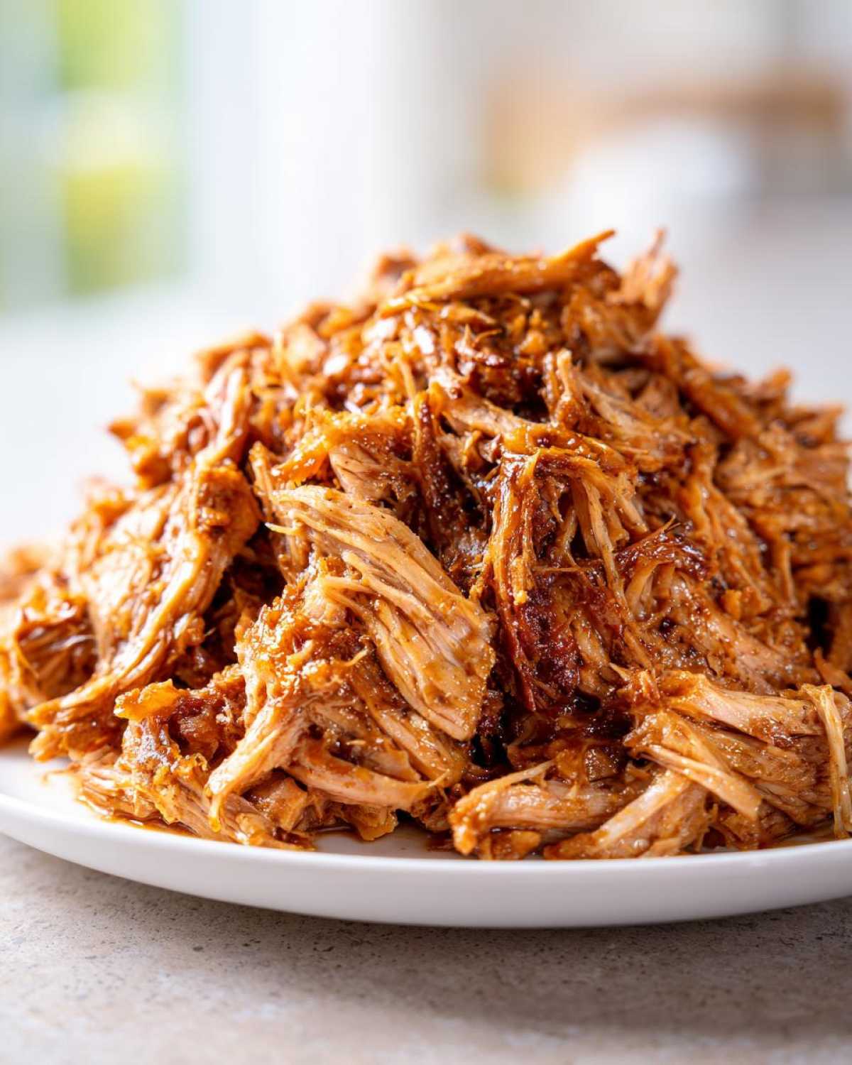 A close-up of a mound of saucy, shredded crock pot pulled pork piled high on a white plate.