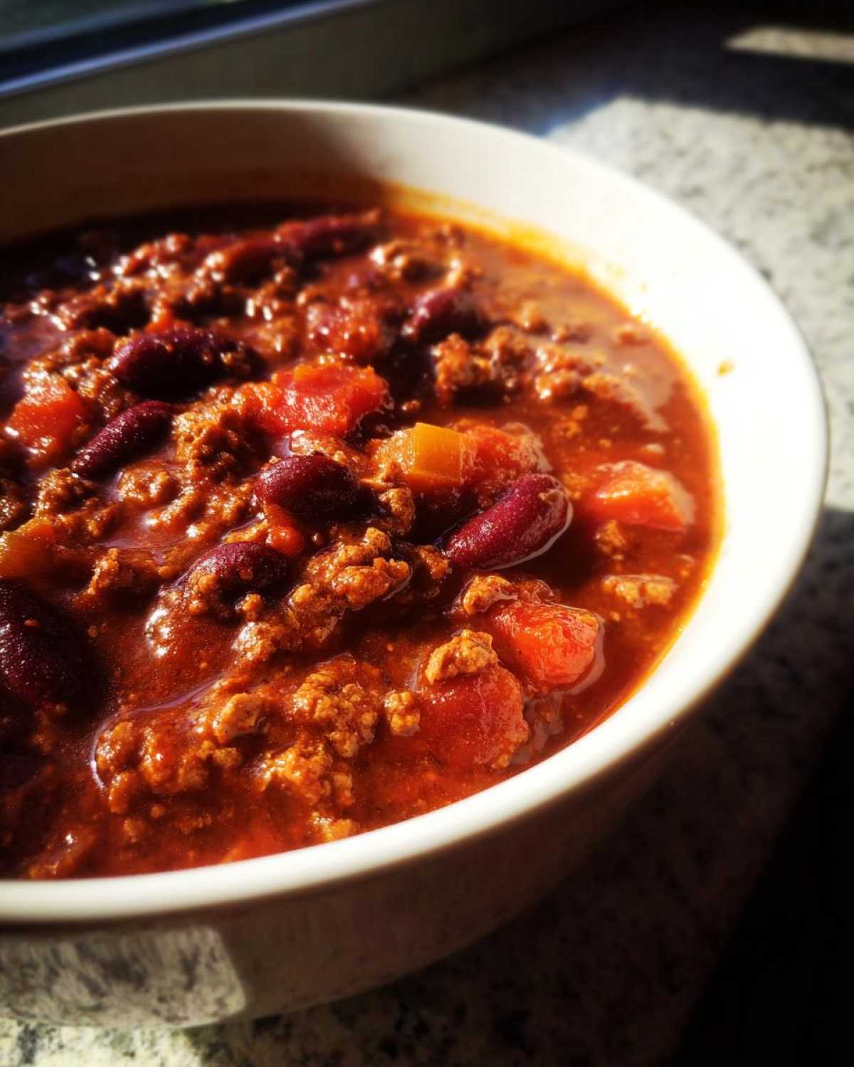 Close-up of a steaming bowl of rich, red crockpot chili filled with ground beef and kidney beans.