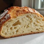 Close-up of a freshly baked french bread loaf cut in half, showing an open, airy crumb structure.