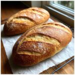 Two golden-brown, crusty loaves of freshly baked French bread cooling on parchment paper.