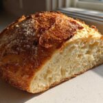 Close-up of a freshly baked Italian bread loaf cut in half, showing a golden, crusty exterior and an airy, open crumb structure.