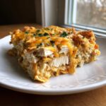 Close-up of a hearty slice of Dorito Casserole showing layers of shredded chicken, creamy sauce, and melted cheddar cheese.