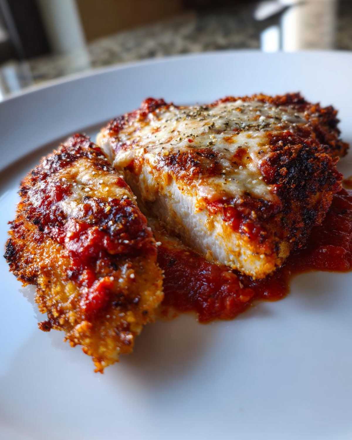 Close-up of Easy Chicken Parmesan cut in half, showing crispy breading, white chicken meat, marinara sauce, and melted mozzarella cheese.