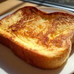Close-up of a single, thick slice of golden brown easy french toast on a white plate.