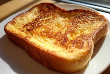 Close-up of a single, thick slice of golden brown easy french toast on a white plate.