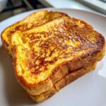Close-up of two golden brown slices of easy french toast stacked slightly on a white plate, glistening with syrup.