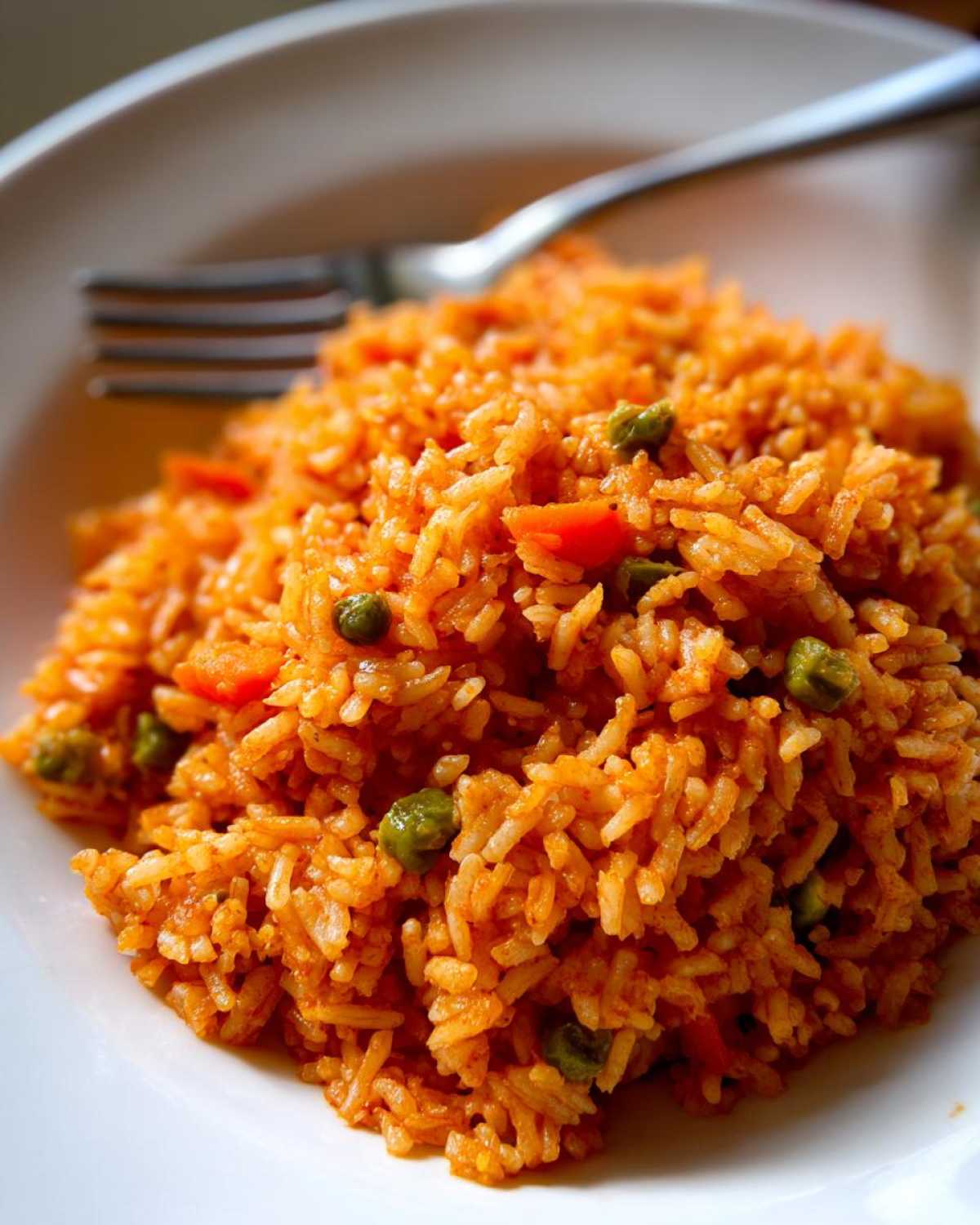 A close-up shot of a serving of bright orange spanish rice mixed with green peas on a white plate.