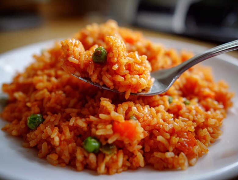 A spoonful of bright orange spanish rice mixed with green peas being lifted from a white plate.