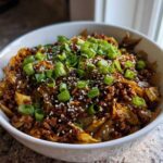 A close-up of a white bowl filled with savory egg roll in a bowl mixture, topped with green onions and sesame seeds.