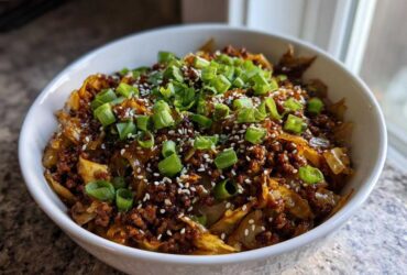 A close-up of a white bowl filled with savory egg roll in a bowl mixture, topped with green onions and sesame seeds.
