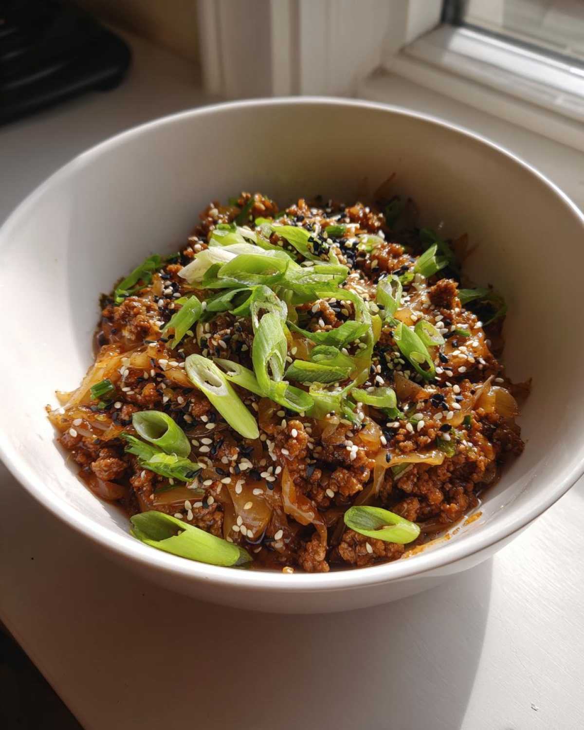 Close-up of a white bowl filled with savory egg roll in a bowl mixture, topped with sliced green onions and sesame seeds.
