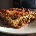 Close-up of a rich, layered slice of zucchini lasagna featuring meat sauce and melted cheese.