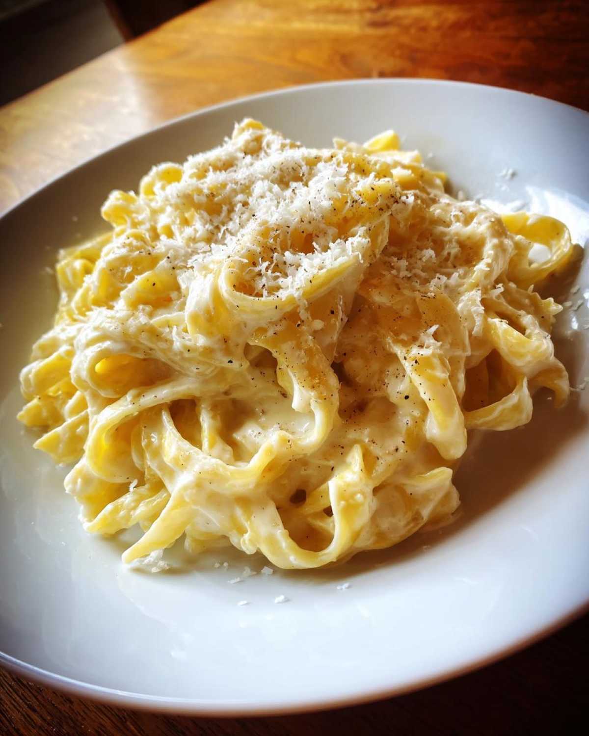 Close-up of fettuccine pasta coated in rich homemade alfredo sauce, topped with grated cheese and black pepper.