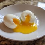 Two perfectly cooked poached eggs cut open on a white plate, showing bright yellow runny yolks spilling out.