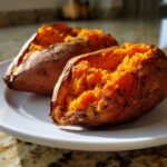 Two perfectly baked sweet potato halves showing fluffy, bright orange insides seasoned with pepper.