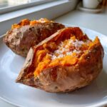 Two perfectly baked sweet potatoes split open and topped with coarse sea salt.