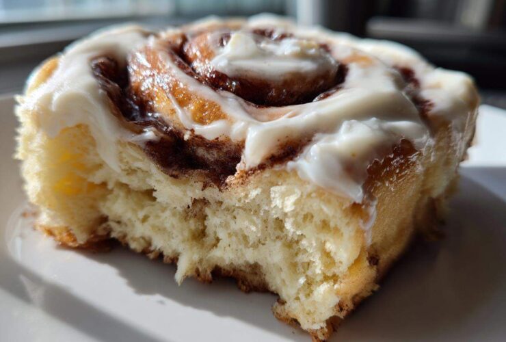 A close-up, cross-section view of a fluffy, homemade cinnamon roll topped with thick white frosting.