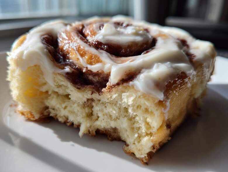 A close-up, cross-section view of a fluffy, homemade cinnamon roll topped with thick white frosting.