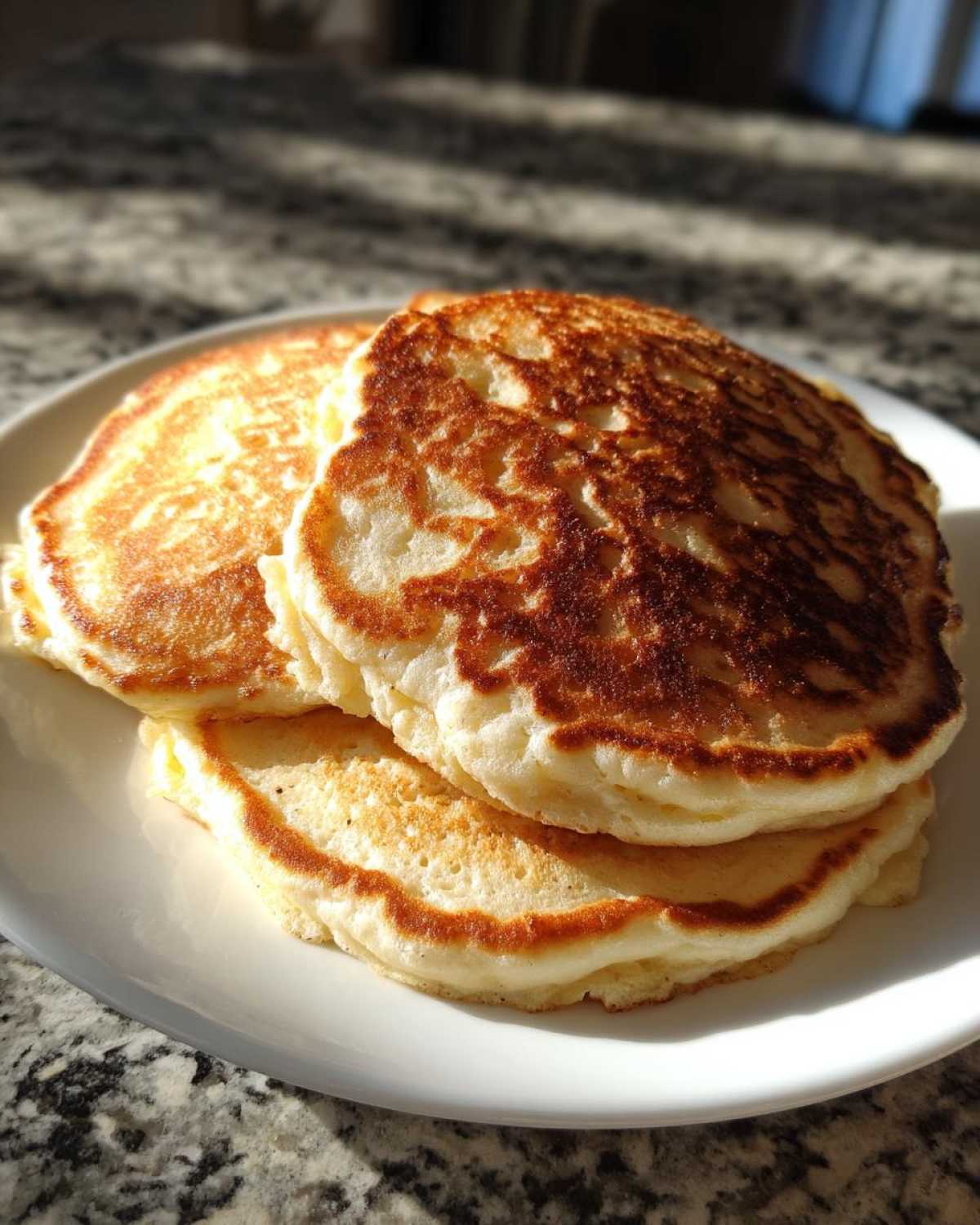 A close-up stack of three fluffy greek yogurt pancakes with golden-brown edges on a white plate.