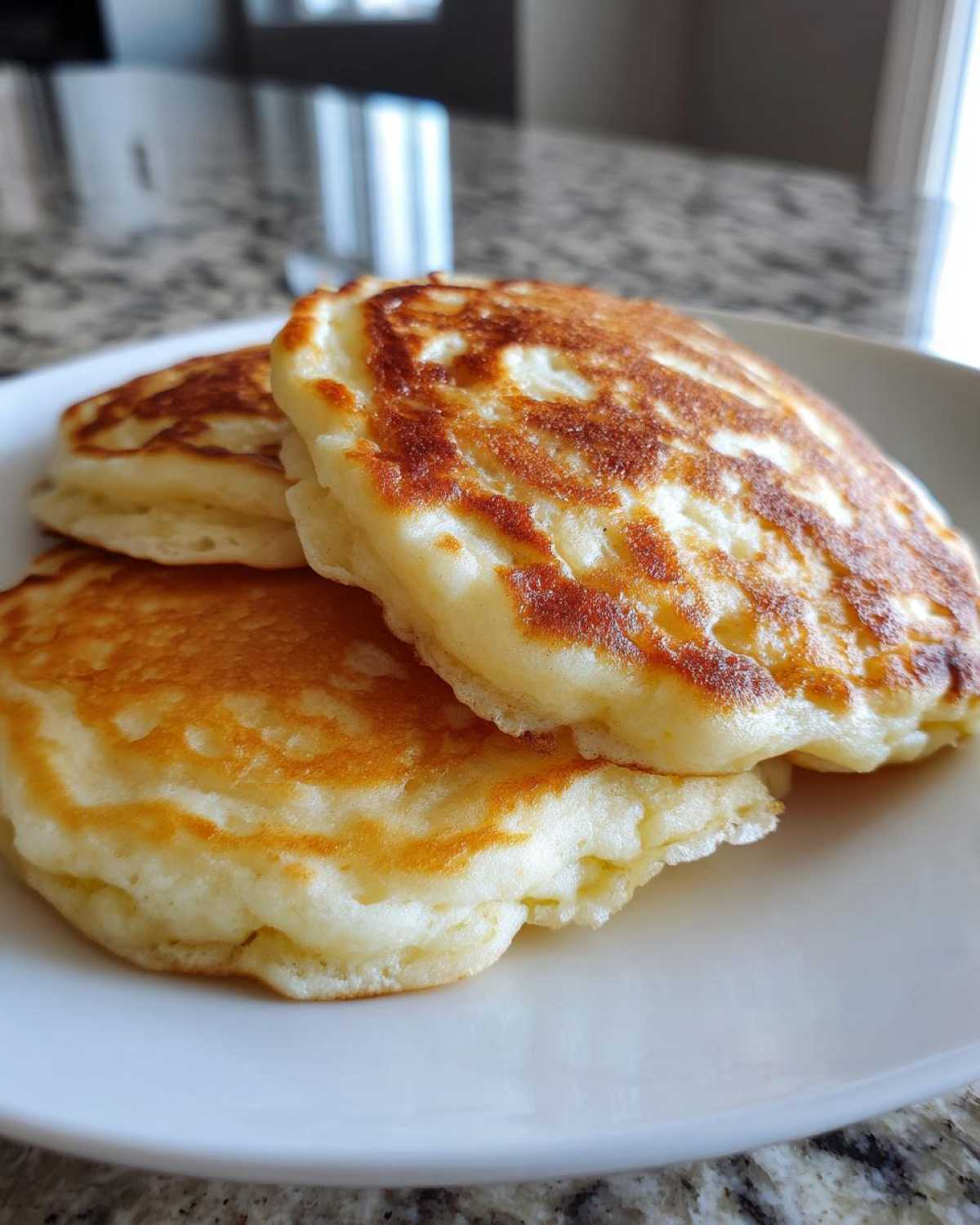 Close-up of three fluffy, golden-brown greek yogurt pancakes stacked on a white plate.