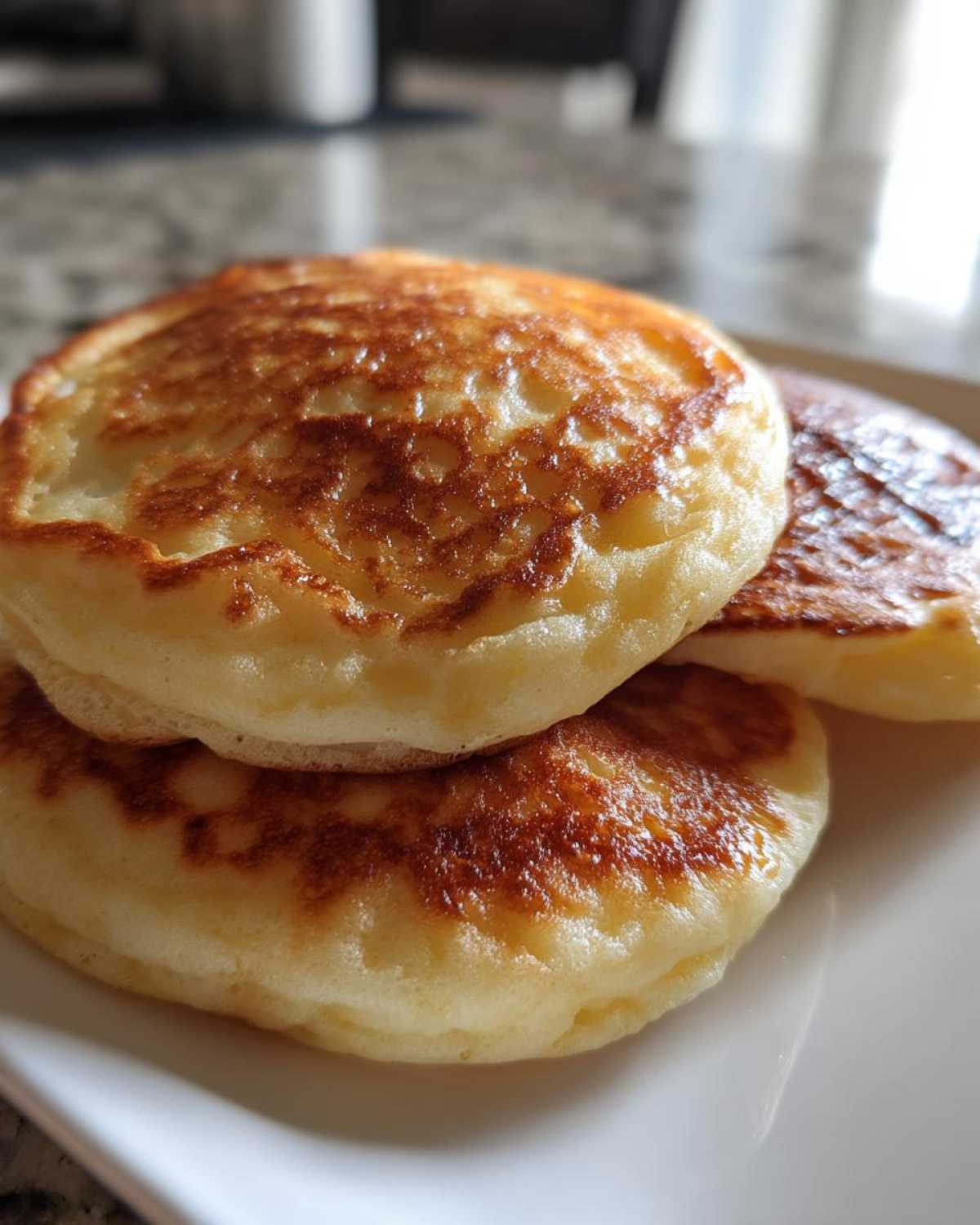 Close-up of a stack of three thick, fluffy greek yogurt pancakes with golden brown tops on a white plate.